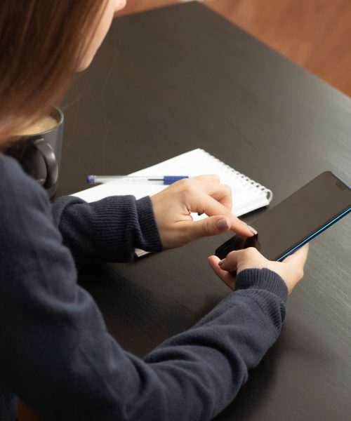girl with a smartphone at a table in a cafe with coffee and a notebook in office clothes